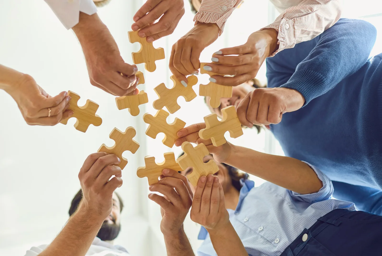 Several hands fitting wooden puzzle pieces together, representing routines being rebuilt piece by piece.