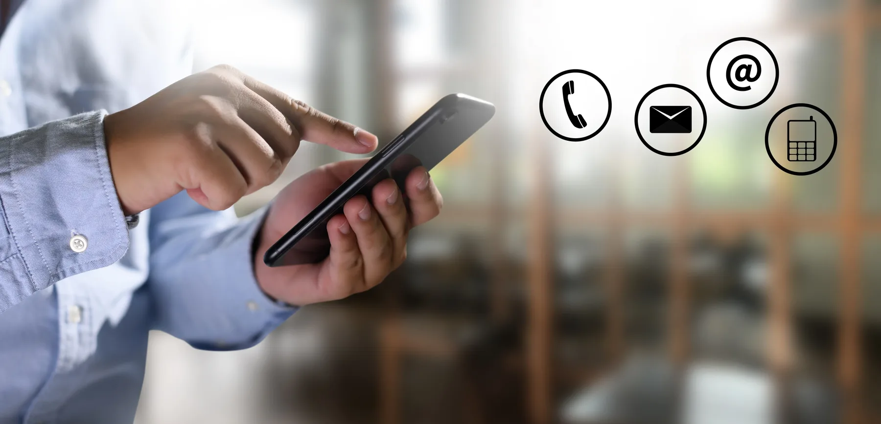 A person holding a mobile phone beside phone, email and message symbols, representing ways to get in touch.
