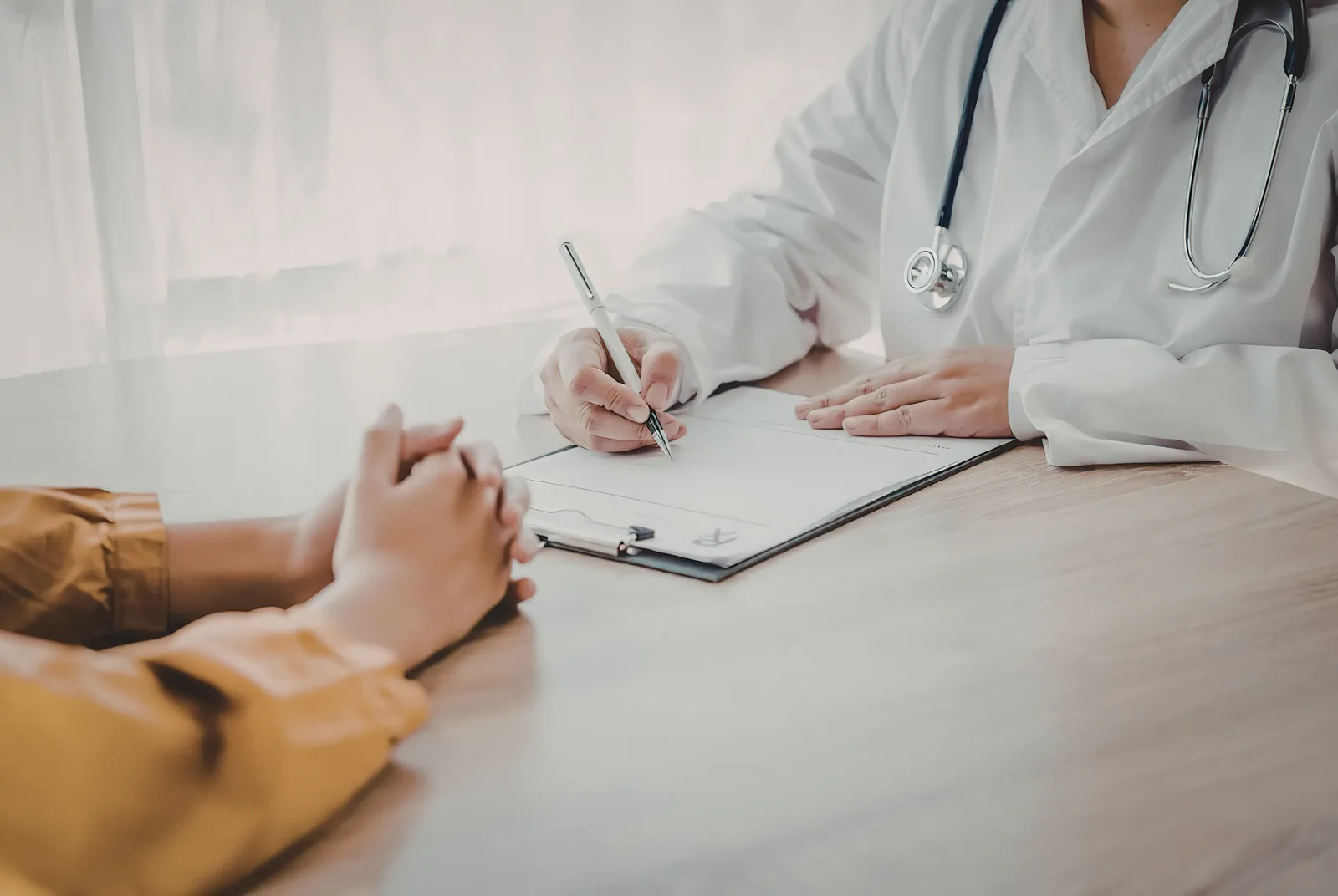 A person in consultation with a healthcare professional who is making notes at a desk.