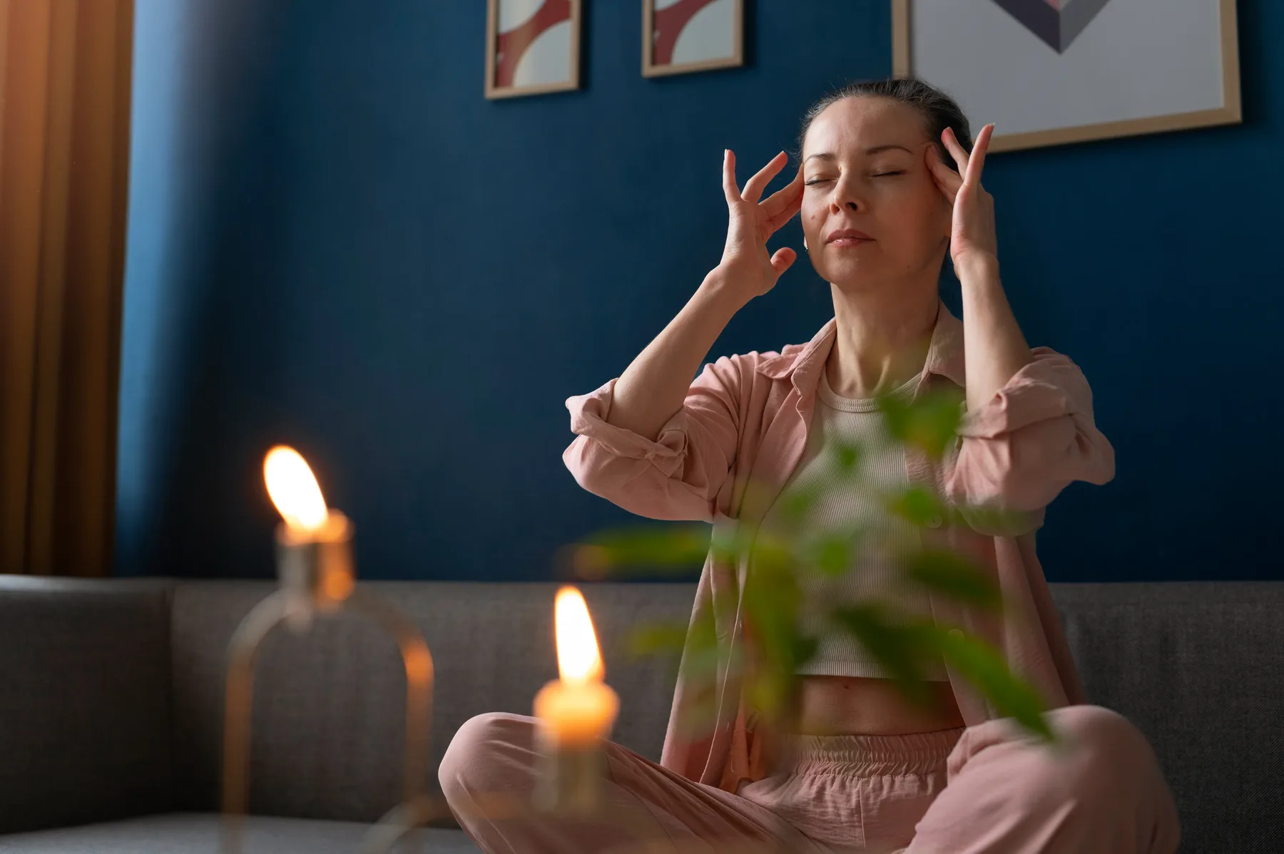 A person sitting cross-legged on a sofa with eyes closed and candles nearby, taking a calm pause.